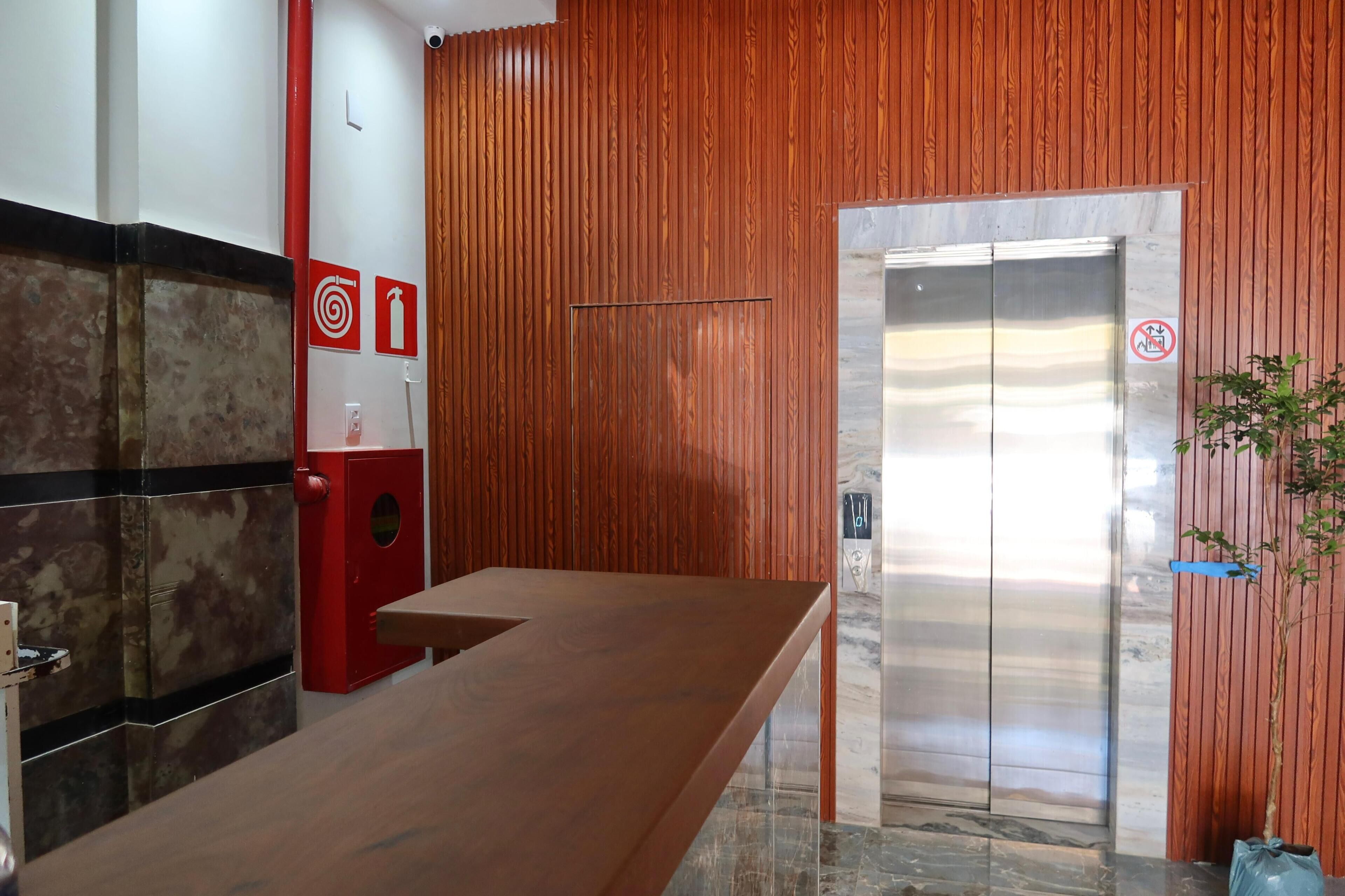 Un espace d’accueil avec un mur en bois, un extincteur rouge, un panneau indiquant la présence d’une cible et d’une borne d’incendie, ainsi qu’un ascenseur.
