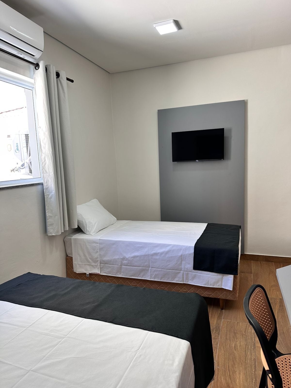 Quarto de hotel com duas camas, uma televisão de tela plana na parede e uma janela com cortinas.