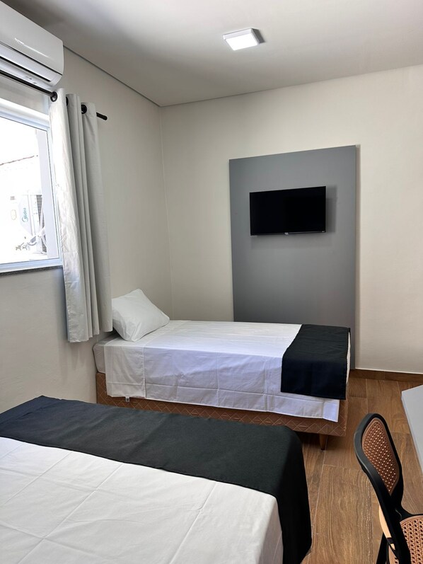 Habitación de hotel con dos camas, un televisor de pantalla plana montado en la pared y una ventana con cortinas.