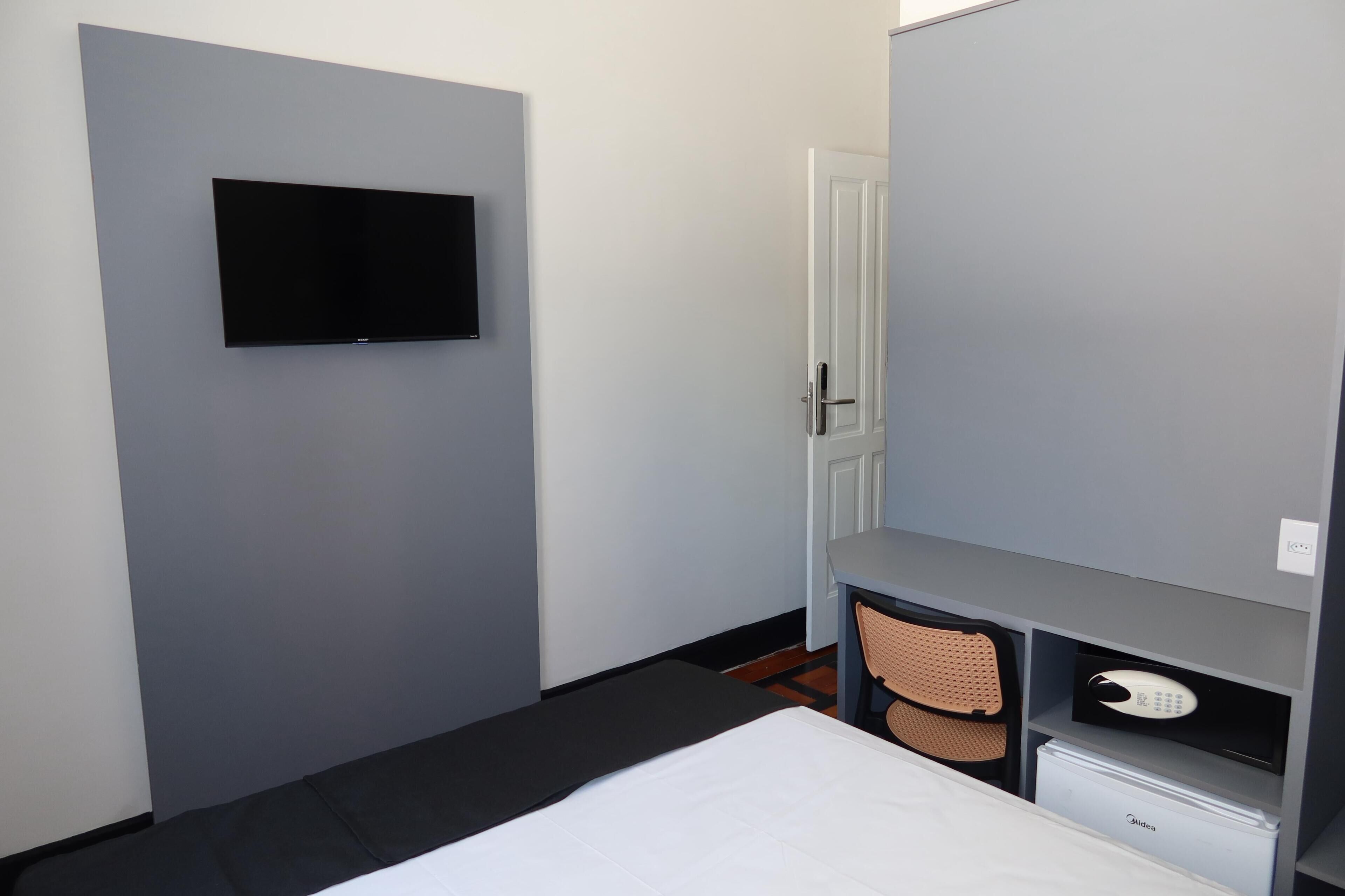 A hotel room with a bed, a desk, a chair, a television, and a minibar.
