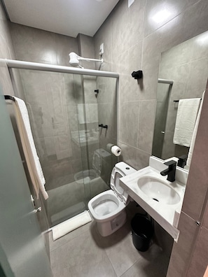 Un baño moderno con ducha envuelta en vidrio, inodoro, lavamanos y espejo.