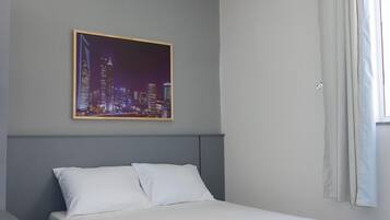 Quarto de hotel com cama, escrivaninha, cadeira, pintura de paisagem urbana e janela com cortinas.