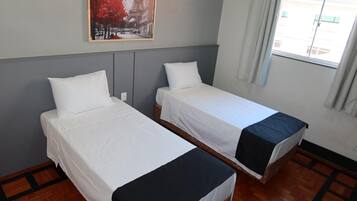 A hotel room with two single beds, a window with curtains, a wooden floor, and a painting on the wall.
