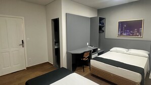 A hotel room with two beds, a desk, a chair, a wardrobe, and a cityscape picture on the wall.