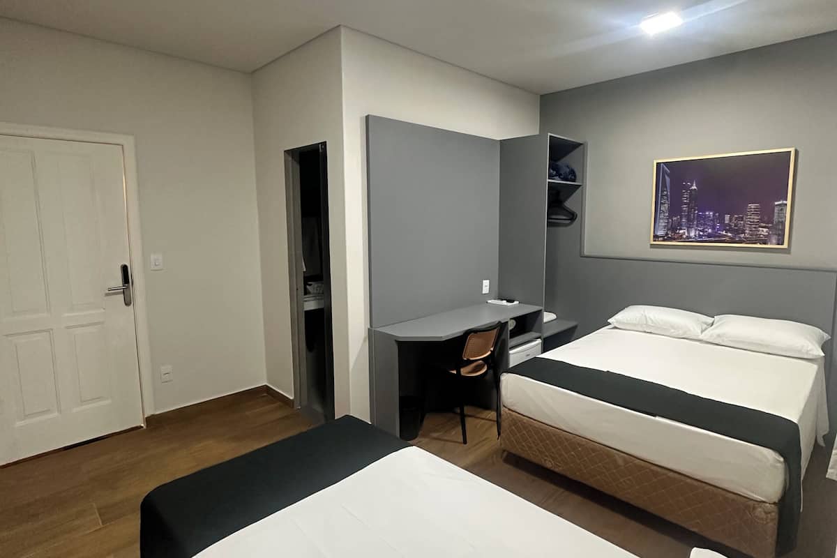 Une chambre d’hôtel avec deux lits, un bureau, une chaise, une armoire et un tableau représentant un paysage urbain accroché au mur.
