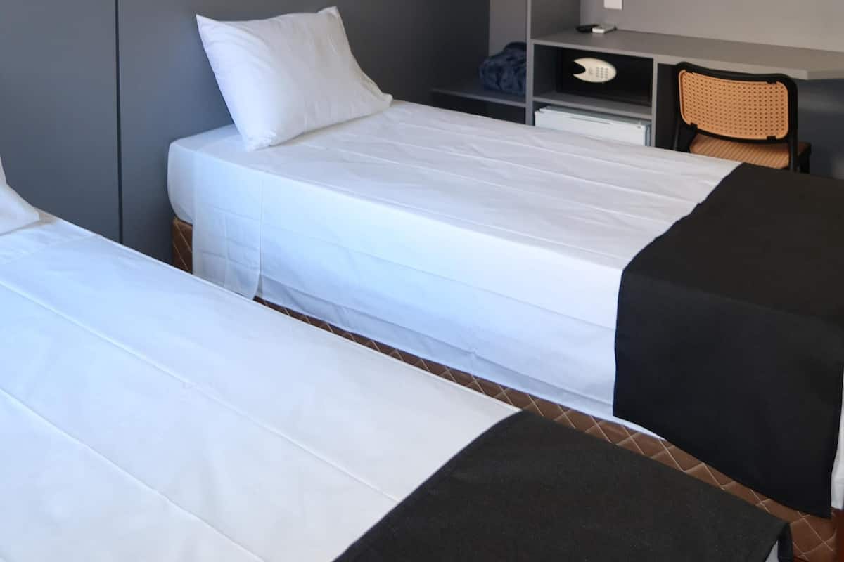 Une chambre d’hôtel avec deux lits, un bureau, une chaise et une armoire.