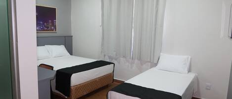 A hotel room with two beds, a desk, a window with curtains, and a cityscape view.