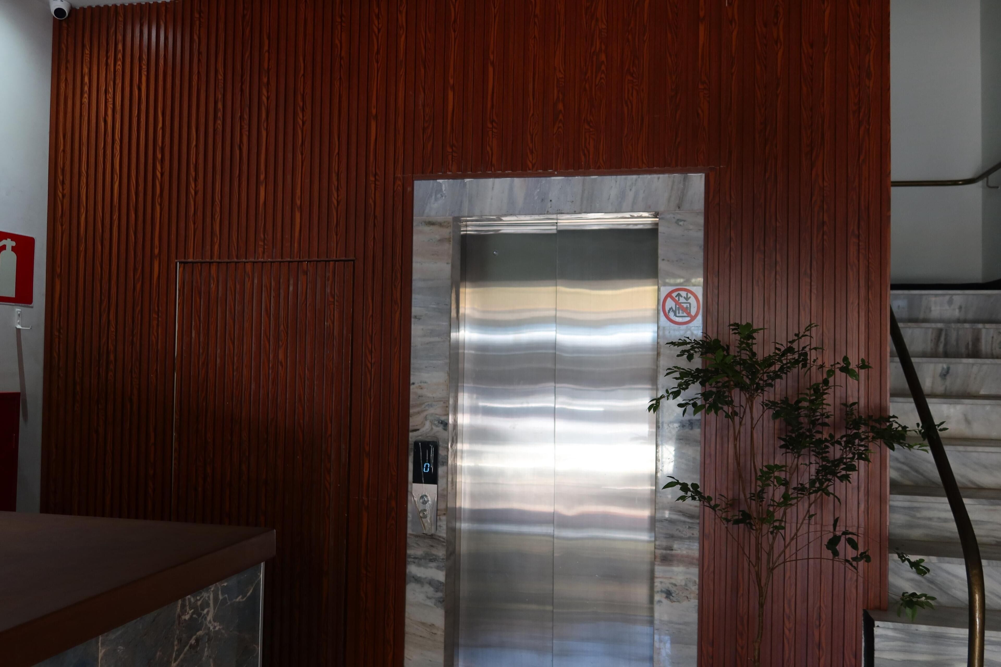 An elevator with a stainless steel finish, a no-smoking sign, and a wooden panel wall.