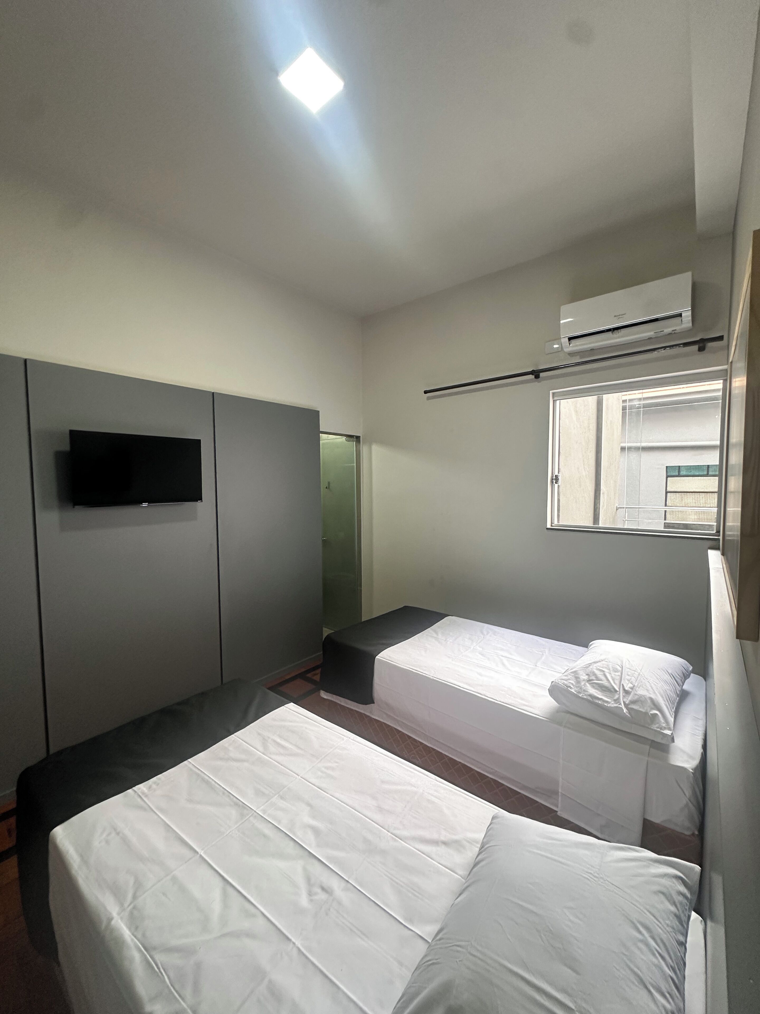 Quarto com duas camas, televisão de tela plana, ar-condicionado e janela com vista.