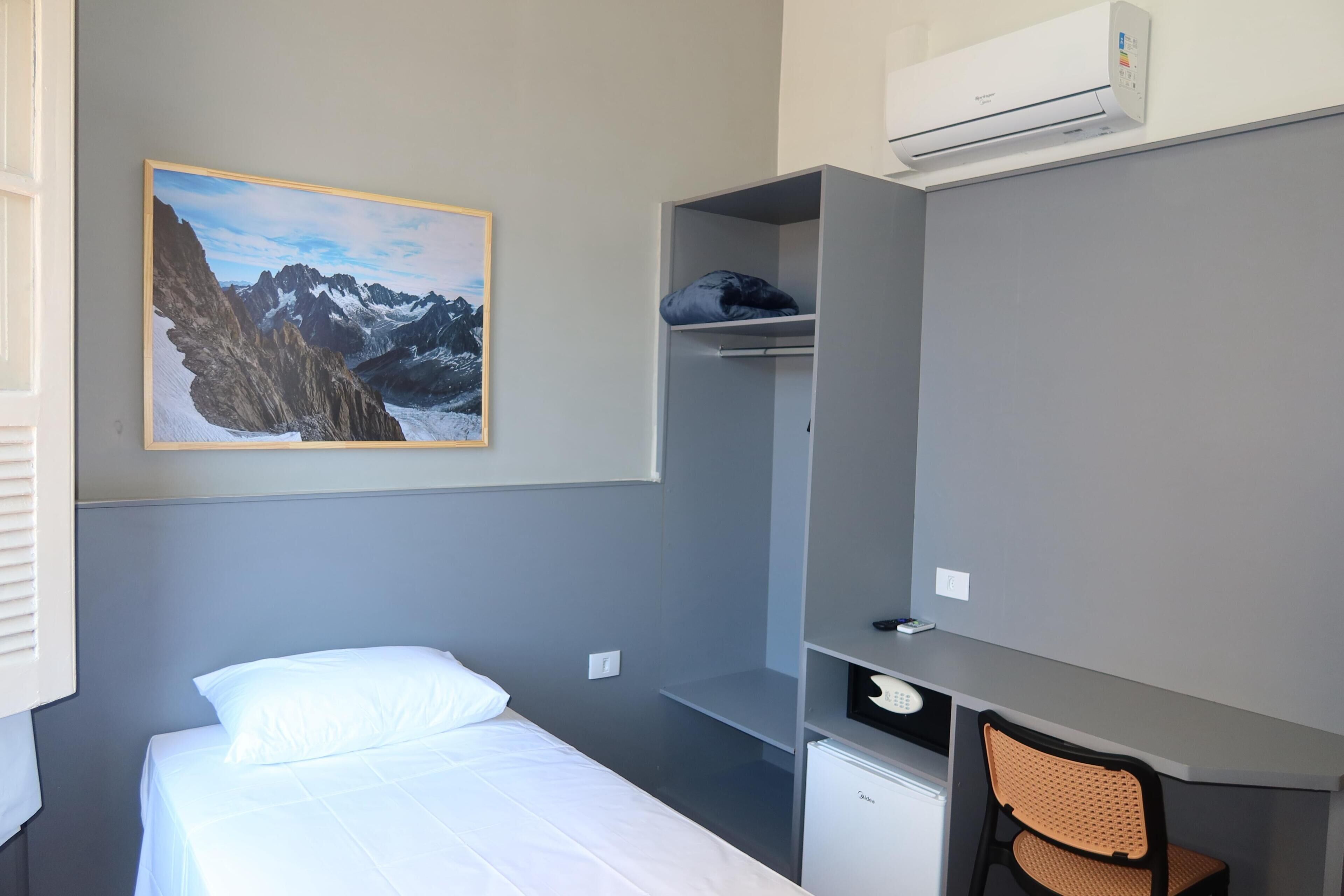 Un dormitorio con cama, escritorio, silla, armario y un cuadro de montañas.