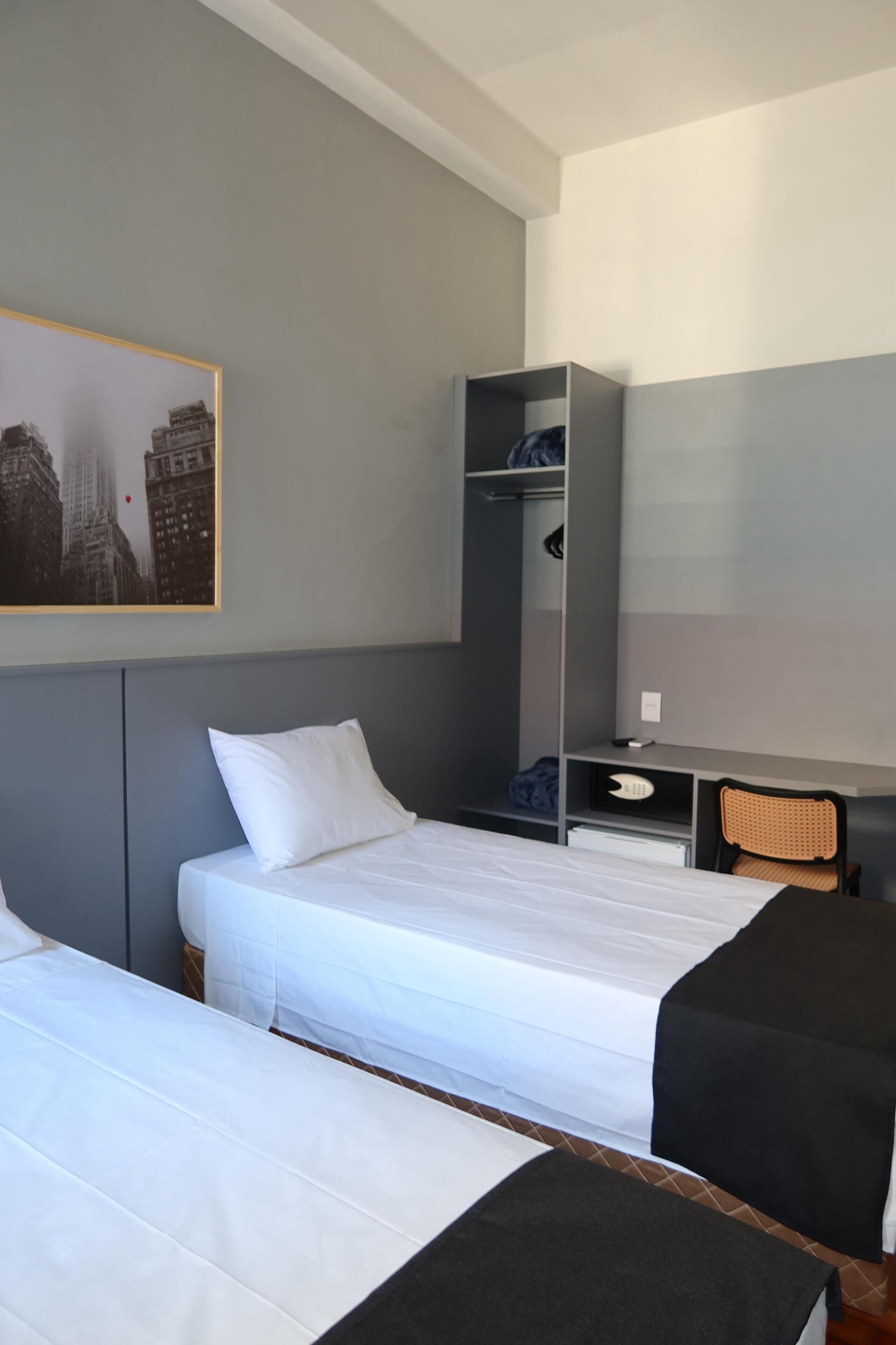 A hotel room with two beds, a desk, a chair, and a wardrobe.