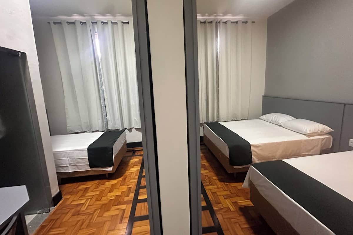 Une chambre d’hôtel avec deux lits, un parquet en bois et des rideaux blancs.