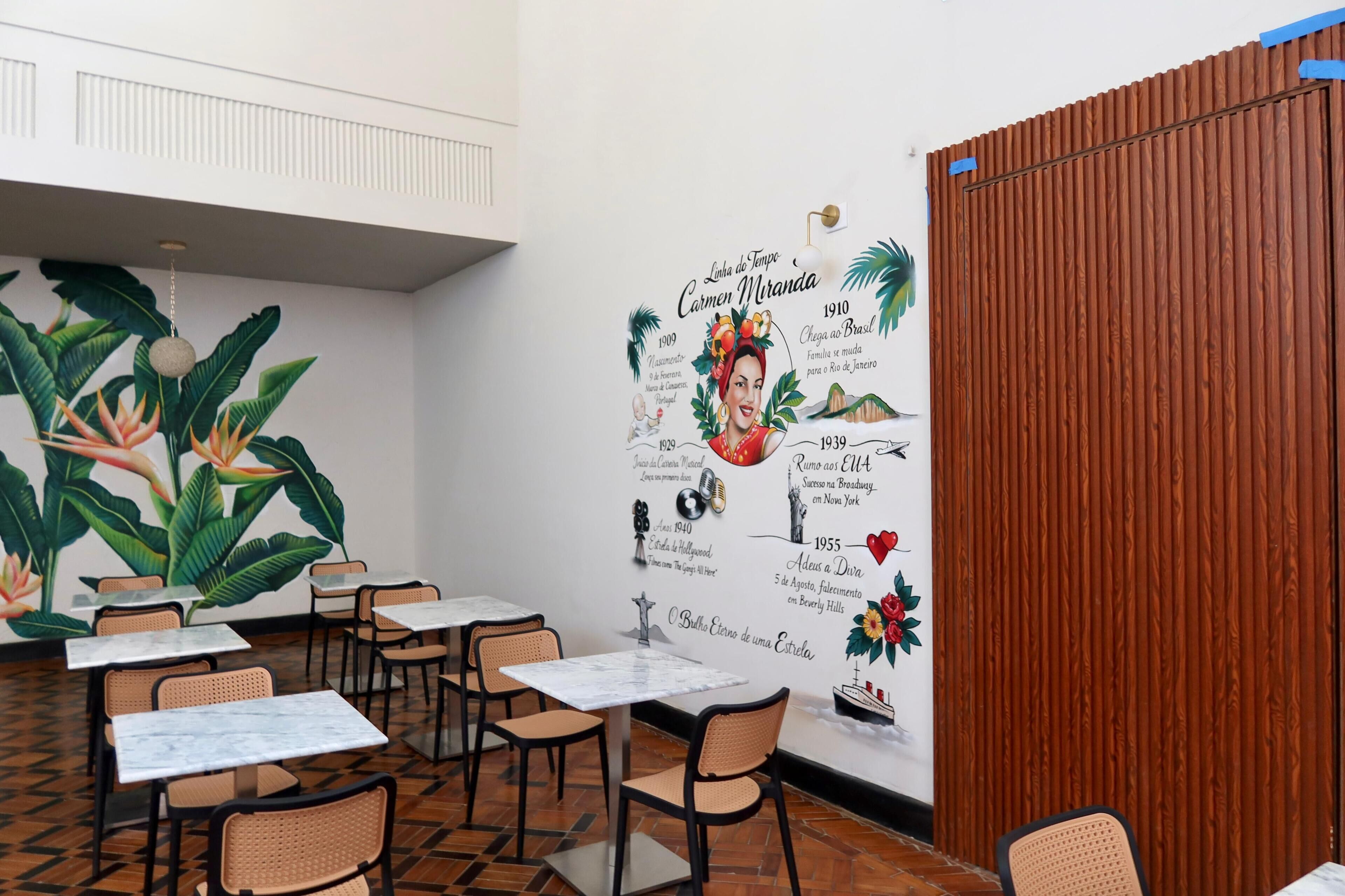 A dining area with tables and chairs, a mural with text and images, and a wooden partition.
