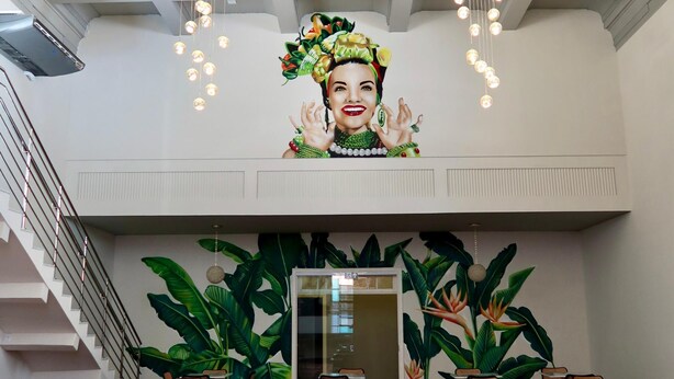 A spacious dining area with multiple tables and chairs, a patterned floor, and a large mural on the wall.