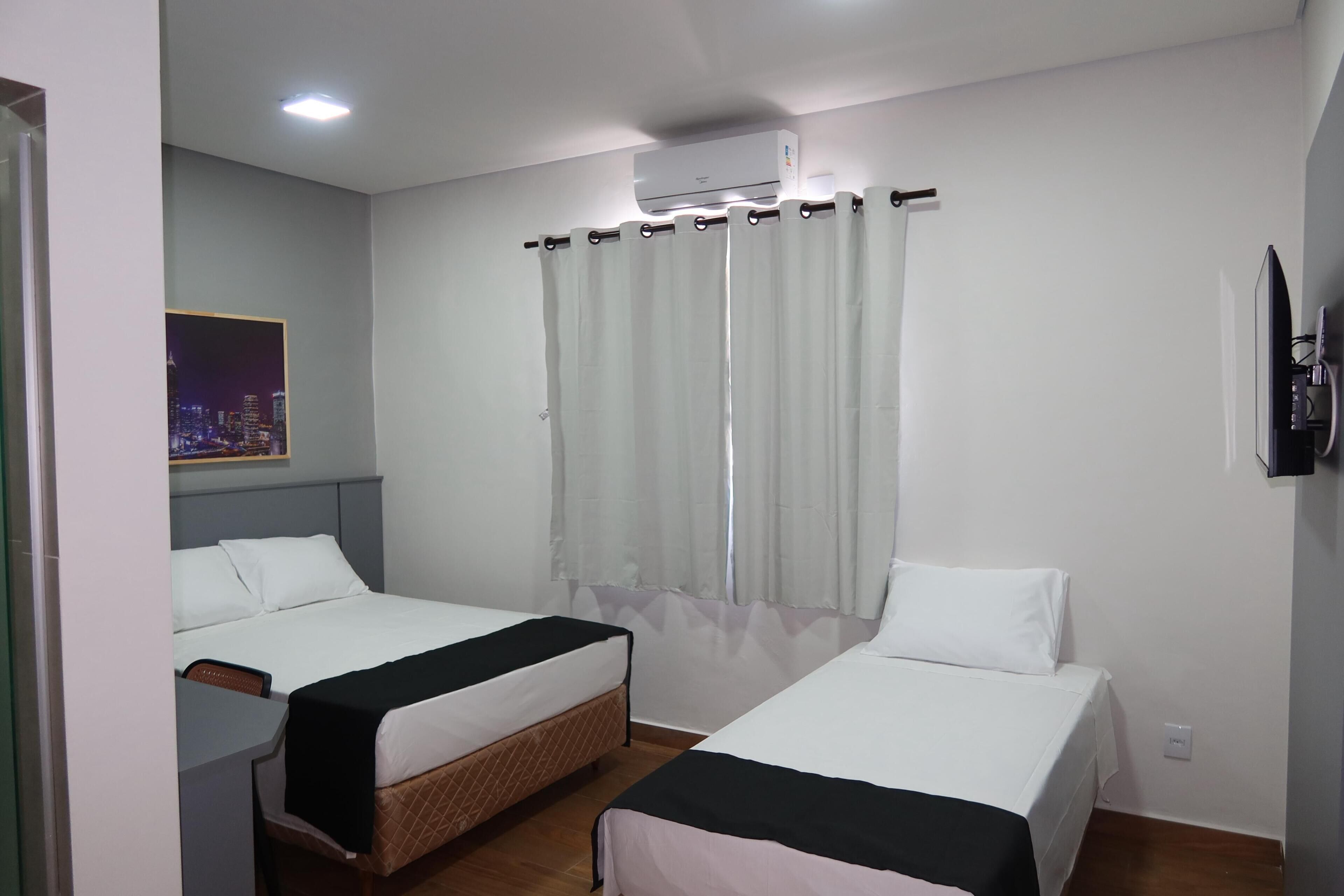 A hotel room with two beds, a cityscape poster, an air conditioning unit, and a television.