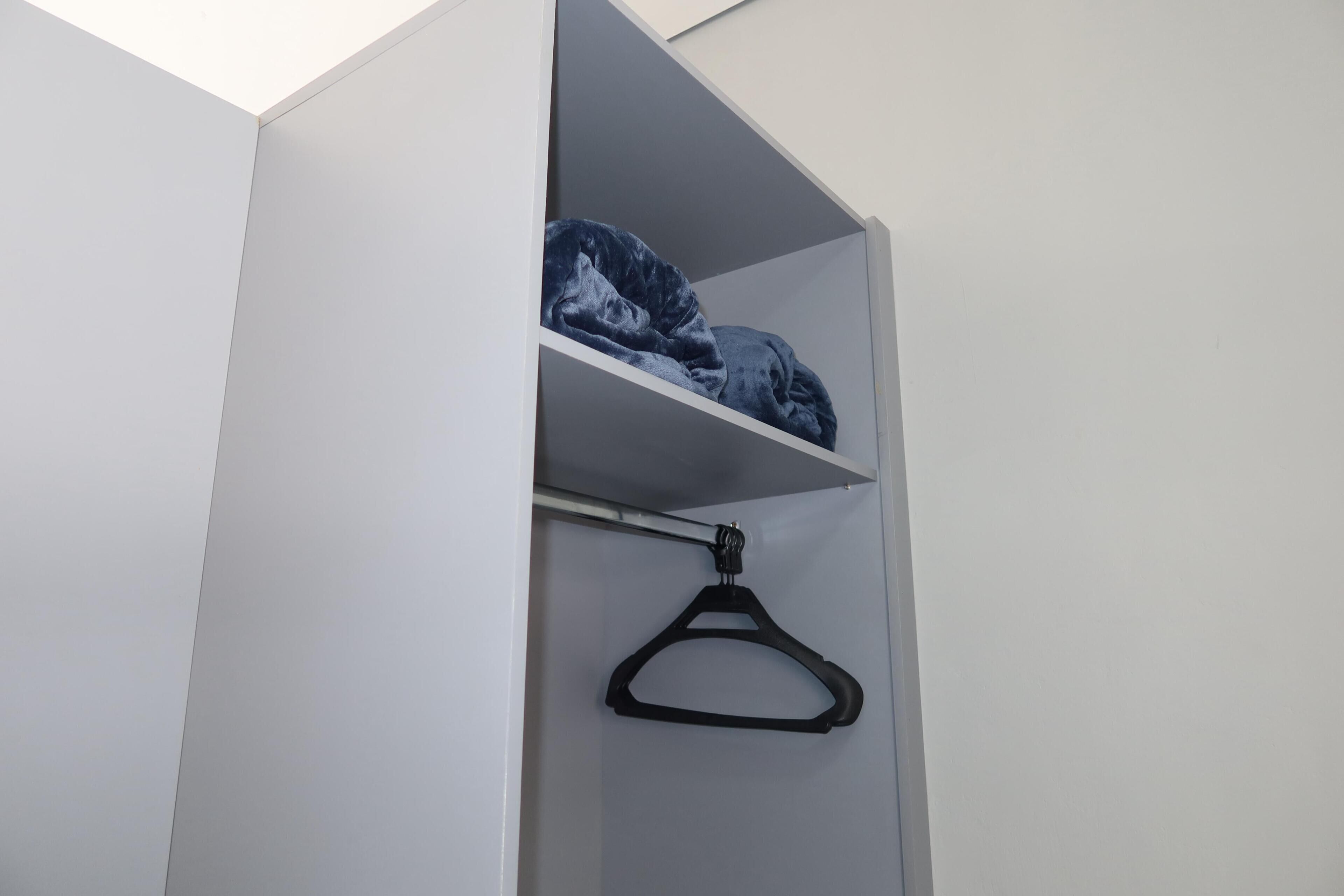 Een witte garderobe met een zwart ophanghaakje en een opgevouwen kledingstuk op de plank.