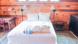 A wooden cabin-style room with a bed, two bedside lamps, a desk, and a chair. - Relaxing Spring Street Cottage with Ocean Views (New Shoreham)