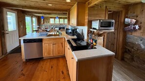 A kitchen with wooden cabinets, a dishwasher, a stove, and a microwave. - Relaxing Spring Street Cottage with Ocean Views (New Shoreham)