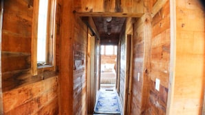 A wooden hallway with a bed at the end, a window on the left, and a door on the right. - Relaxing Spring Street Cottage with Ocean Views (New Shoreham)