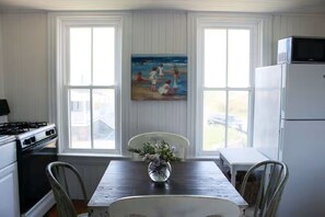 Une cuisine avec une table à manger, des chaises, un tableau et un réfrigérateur.