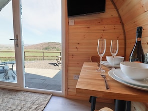 A dining area with a table set for two, a bottle of wine, and a view of a grassy field through a glass door. - Cennin Pedr (Ruthin)
