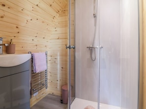 A bathroom with wooden walls, a glass shower enclosure, a sink with a towel, and a toilet. - Cennin Pedr (Ruthin)