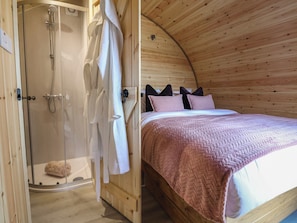 A wooden interior with a shower, a bed with a pink blanket, and a wooden ceiling. - Cennin Pedr (Ruthin)