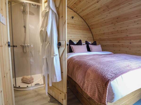 A wooden interior with a shower, a bed with a pink blanket, and a wooden ceiling. - Cennin Pedr (Ruthin)