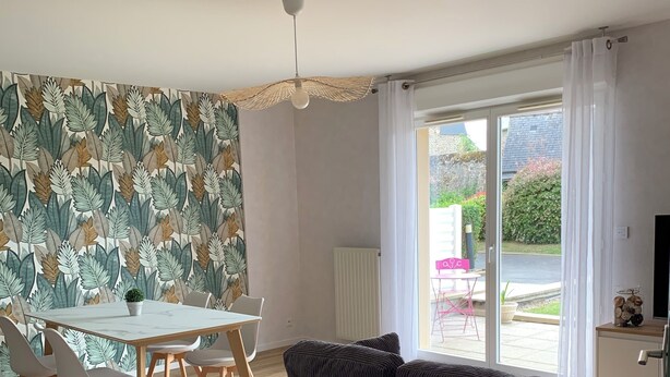 Un salon moderne comprenant un canapé, une table à manger, des chaises et une vue sur l’extérieur grâce à une porte vitrée.