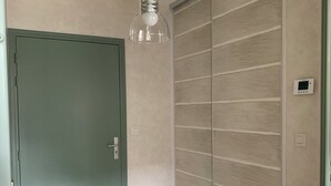 Une pièce avec un plancher en bois, une porte verte, un ventilateur de plafond et un thermostat fixé au mur.