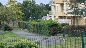 Un immeuble résidentiel doté de nombreux balcons, d’une allée d’accès fermée par un portail et entouré de verdure.