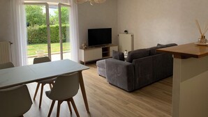 Un salon moderne comprenant un téléviseur, un canapé, une table à manger, des chaises et une porte-fenêtre coulissante donnant sur un jardin.