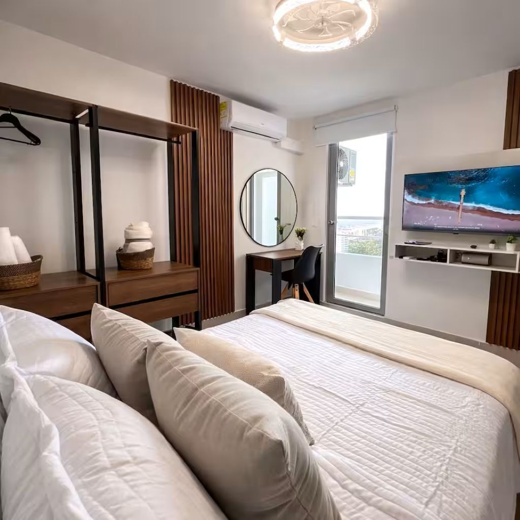 Ein modernes Hotelzimmer mit einem Bett, einem Schreibtisch, einem Sessel, einem Fernseher und einem Balkon.