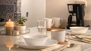 Ein Essbereich mit Kaffeemaschine, weißem Geschirr und einer Kerze.