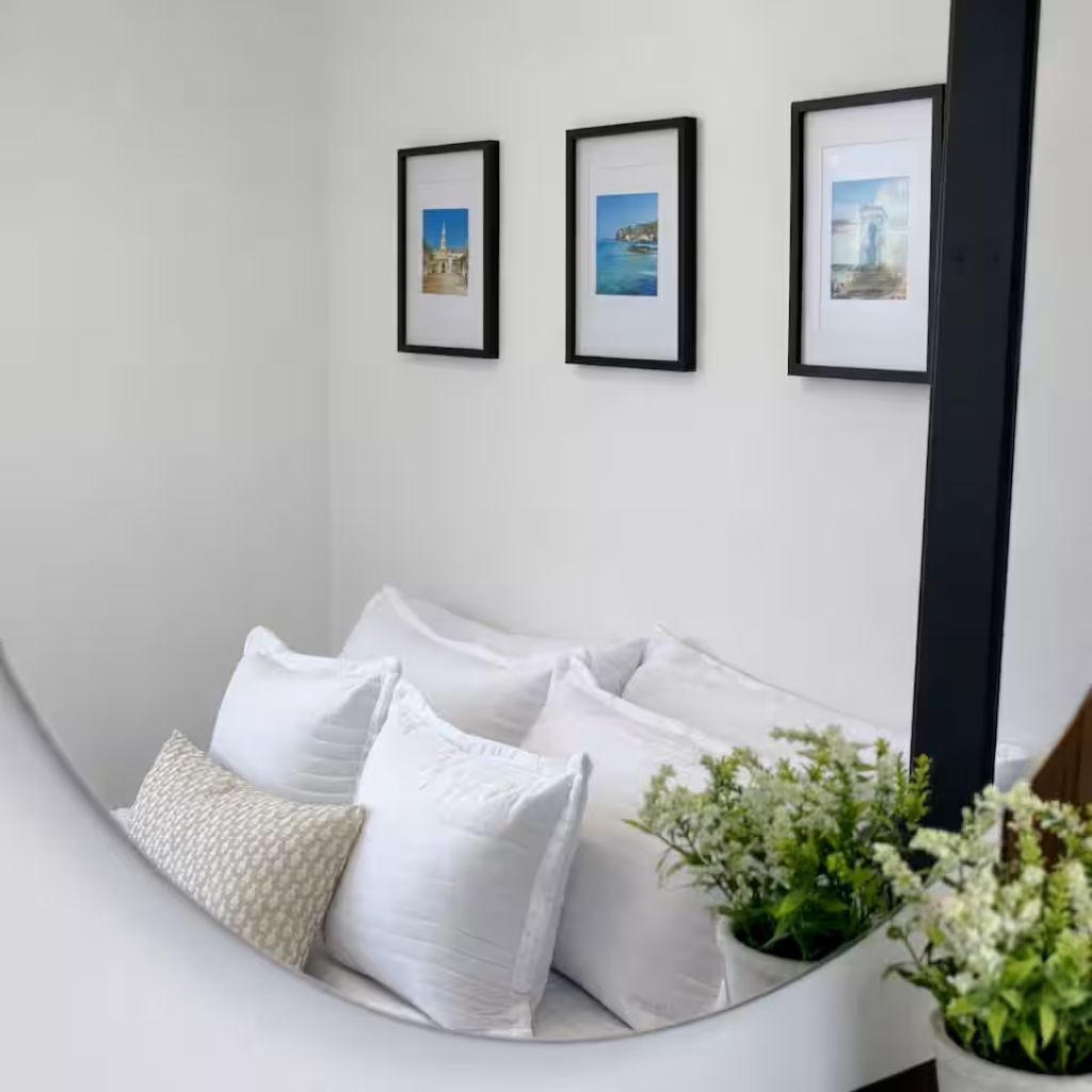 A white sofa with white cushions, a small potted plant, and three framed pictures on the wall.