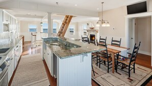 A spacious kitchen with a central island, a dining area with chairs, and a staircase leading to another level.