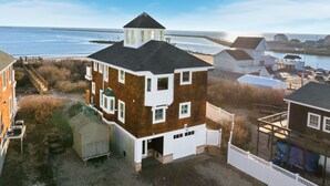 A two-story house with a garage, a small tower-like structure on the roof, and a view of the sea.
