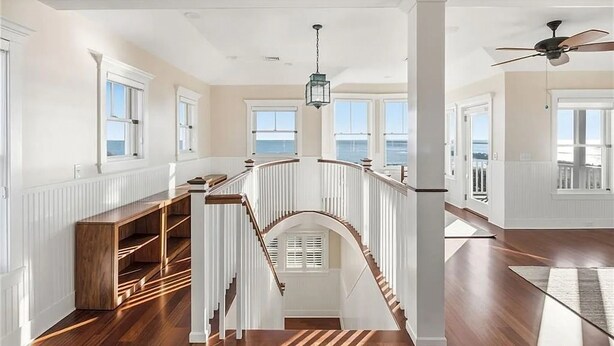 A spacious interior with a wooden staircase, white walls, and large windows.