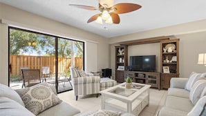 A living room with a sofa, armchair, coffee table, TV, and a ceiling fan. - Beautiful Townhome/Fully Furnished in the heart of Palm Harbor. (Palm Harbor)