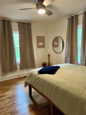Ein Schlafzimmer mit Bett, Deckenventilator, Gitarre und Vorhängen.