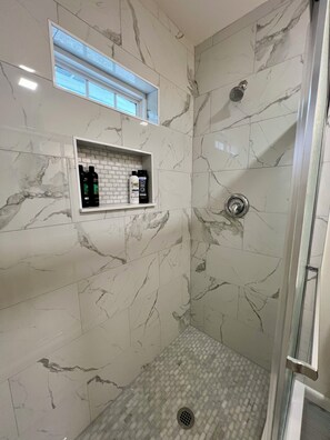 Eine Dusche mit Glastür, Marmorwänden und Ablage für Toilettenartikel.
