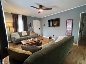 Una sala de estar con sofá, una mesa de centro, televisor y ventilador de techo.