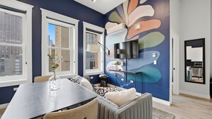 Uma sala de estar moderna com área de jantar, janelas amplas e um mural abstrato colorido na parede.