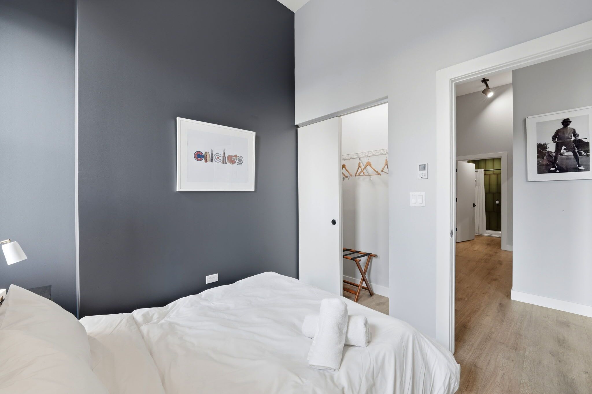 A modern hotel room with a bed, a wall-mounted artwork, a door leading to a hallway, and a framed picture on the wall.