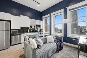 A modern kitchen with white cabinets, stainless steel appliances, and a dining area with a gray sofa and patterned cushions.