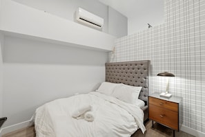 A bedroom with a bed, a nightstand, a lamp, an air conditioner, and a grid-patterned wall.