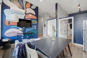 Un comedor moderno con una mesa oscura, sillas, un florero con flores, un televisor montado y una unidad de aire acondicionado en la pared.