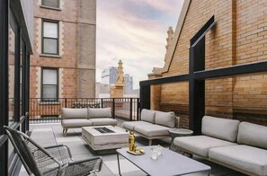 A rooftop patio with outdoor seating, a fire pit, and a view of a city skyline.