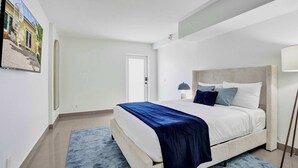 Un dormitorio con cama, lámpara de noche, una puerta y un cuadro en la pared.