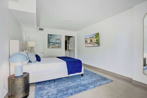 Ein Schlafzimmer mit einem Bett, einer Lampe, einem blauen Teppich und zwei Bildern an der Wand.
